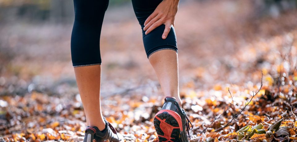 Close-up of sporty woman has muscle injury and holding her painful leg in the forest.
