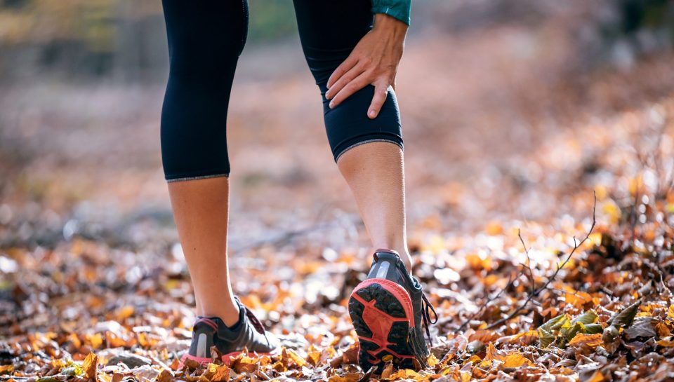 Close-up of sporty woman has muscle injury and holding her painful leg in the forest.