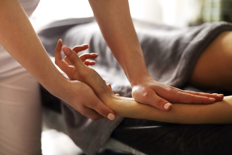 Faceless master massaging arm and wrist of woman lying on table in massage salon